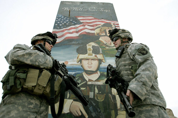 Two US soldiers standing in front of a mural dedicated to a fallen comrade