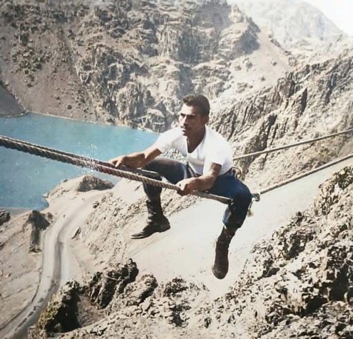 Man sitting between two ropes over a rocky ledge
