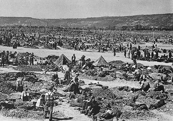 Prisoners of war (POWs) standing around tents and mounds of dirt at the Sinzig prison camp