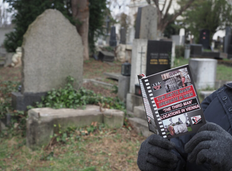 Individual holding 'The Third Man' anniversary booklet in a cemetery