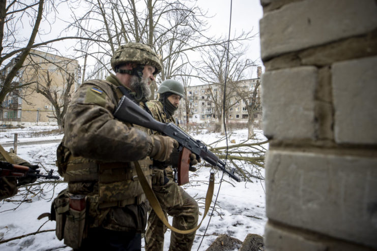 Two Ukrainian soldiers walking past a building with their weapons drawn