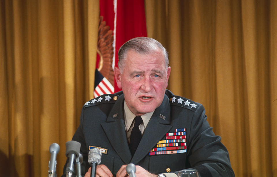 Creighton Abrams speaking at a table lined with microphones