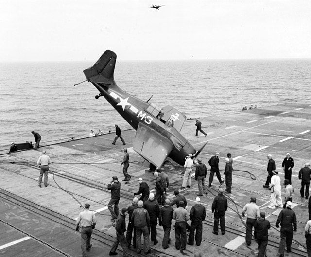 Crewmen standing around a General Motors FM-2 Wildcat that crashed into the flight deck of the USS Sable (IX-64)