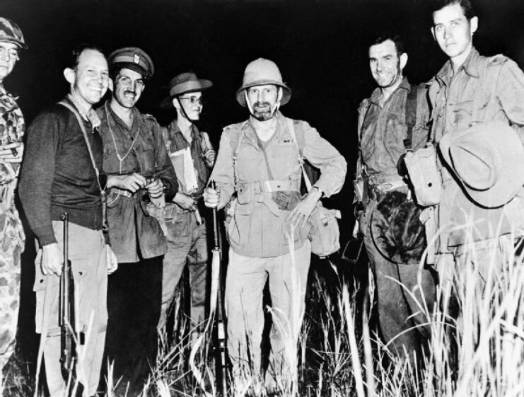 Frank Merrill, J.R. Alison, J.M. Calvert, Capt. Borrow, Orde Wingate, W. Scott and Francis Stewart standing together in tall grass