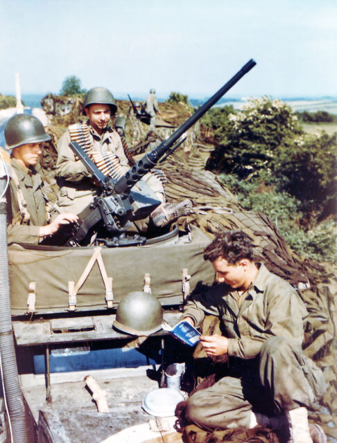 Two American soldiers inspecting an anti-aircraft gun while another reads a book