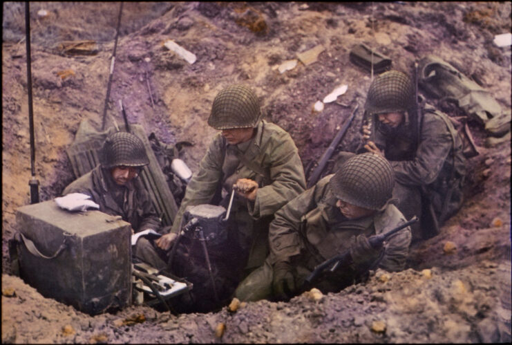 Four members of the US Army Provisional Ranger Group sitting around a radio in a foxhole