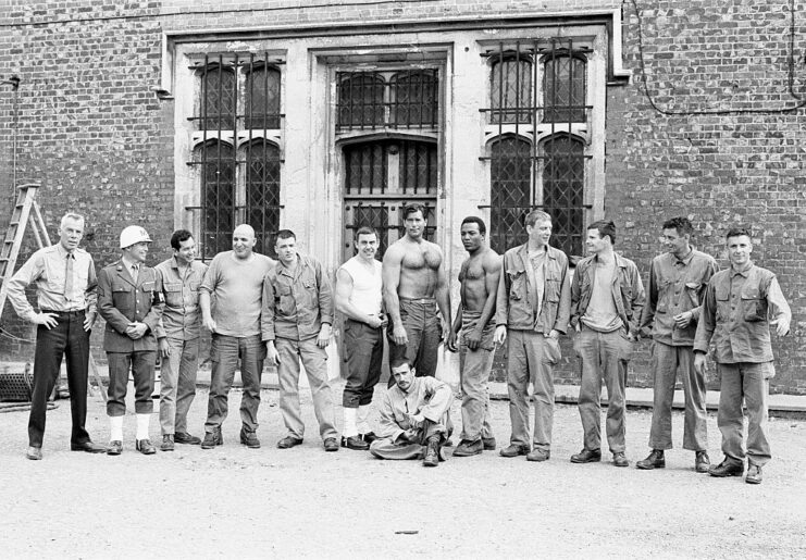 Cast of 'The Dirty Dozen' standing together in front of a brick building