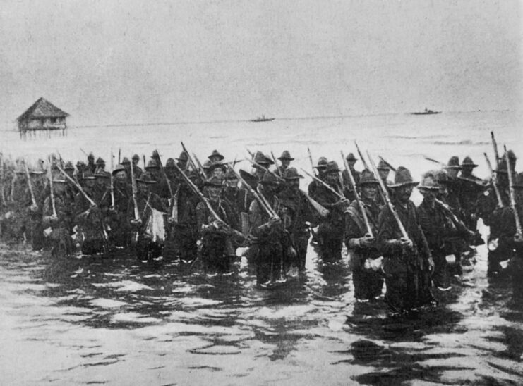 US soldiers wading through water with their rifles resting on their shoulders