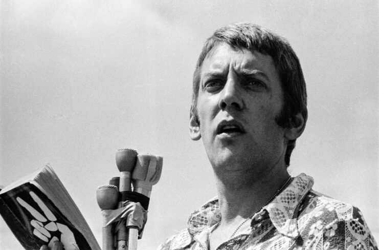 Donald Sutherland reading from 'Johnny Got His Gun' while standing behind a group of microphones