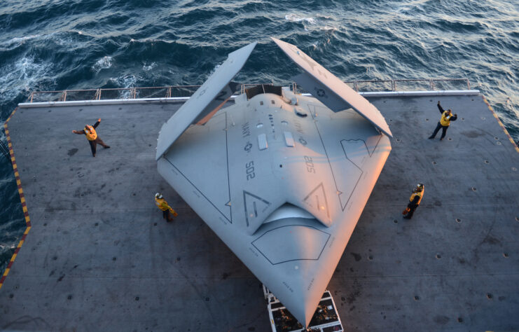 Four crewmen standing around a Northrop Grumman X-47B on the aircraft elevator aboard the USS George H.W. Bush (CVN-77)