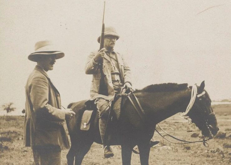 Theodore Roosevelt sitting on horseback while equipped with an M1903 Springfield, with a man standing beside him