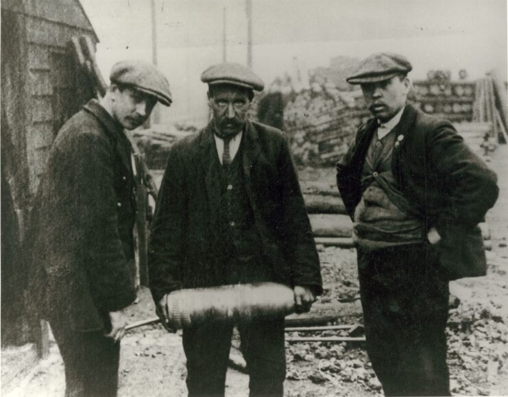 One man holding an unexploded shell while two others stand around him