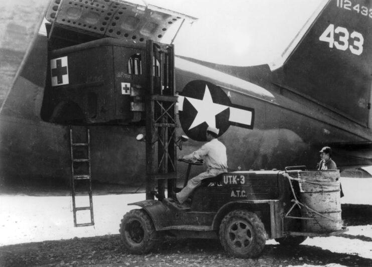 Military personnel operating a forklift to remove the body of an ambulance from a cargo aircraft