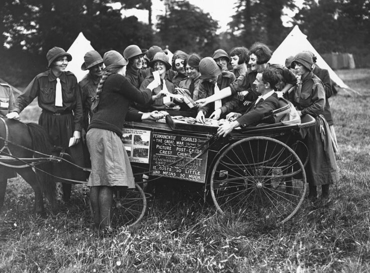 Girl Guides surrounding a soldier sitting in a cart