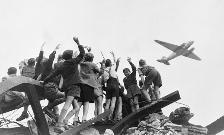 Children waving at an American cargo aircraft flying over them