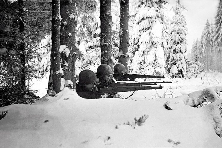 Three American infantrymen aiming their weapons from behind a pile of snow