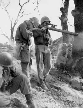 Soldier aiming an M18 recoilless rifle while two others cover their ears