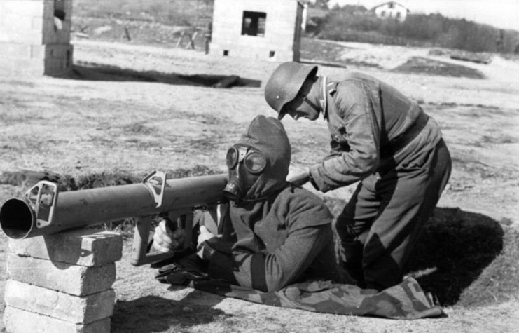 Soldier manning a Panzerschreck in protective gear while another stands behind him