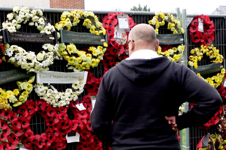 Man standing in front of rows of wreaths made from poppies