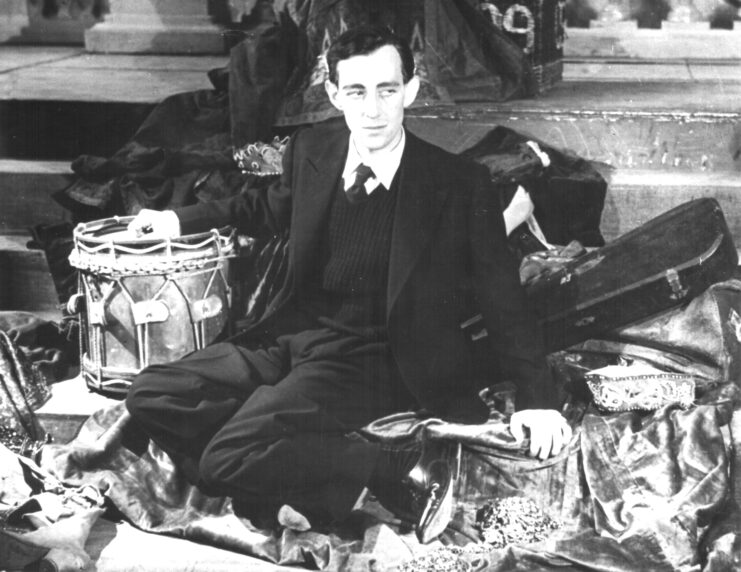 Alec Guinness sitting on a pile of props