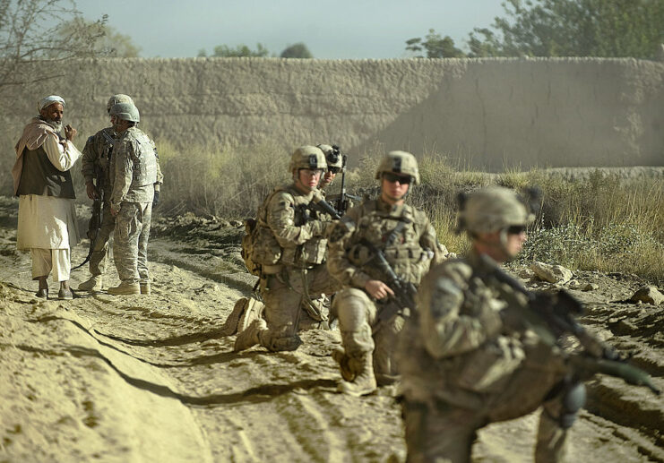 US Army soldier and an interpreter speaking with an Afghan man while four other soldiers position themselves nearby