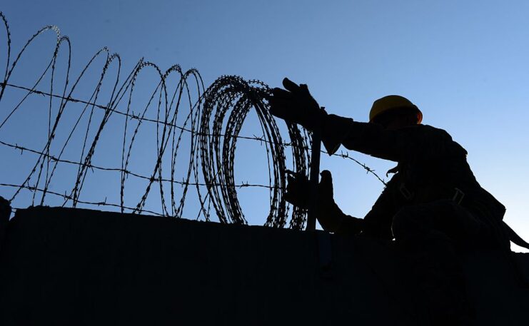 US Army soldier removing barbed wire from the top of a wall