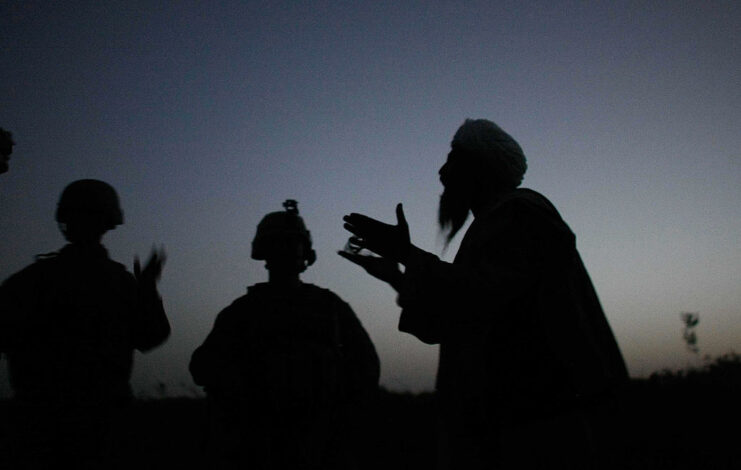 Two US Marines speaking to an Afghan man at dusk