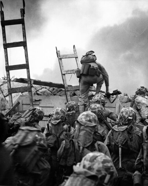 1st Lt. Baldomero Lopez climbing over a seawall while other Marines follow suit