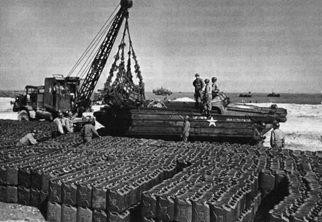 Crane lifting a DUKW while Allied servicemen stand atop it