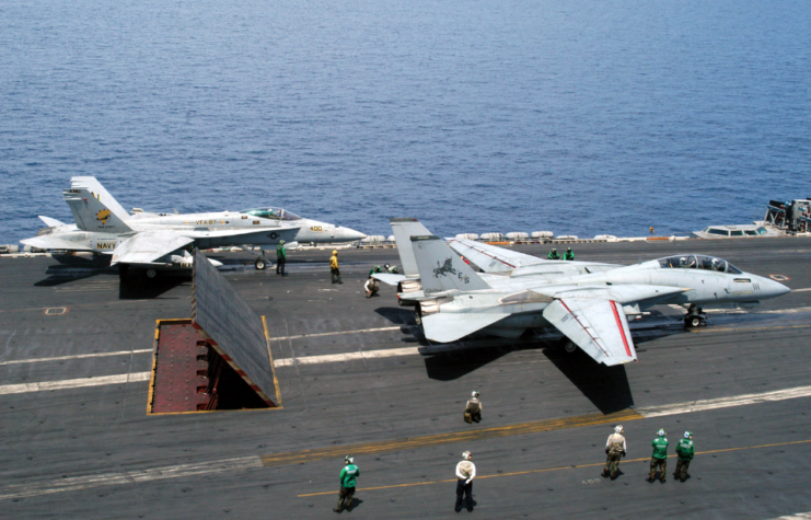 Crewmen walking past a McDonnell Douglas F/A-18 Hornet and a Grumman F-14D Tomcat on the flight deck of the USS Theodore Roosevelt (CVN-71)