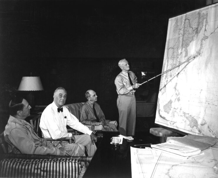 Franklin Roosevelt, William Leahy and Douglas MacArthur looking at Chester Nimitz pointing at a large map of the Pacific Ocean and East Asia