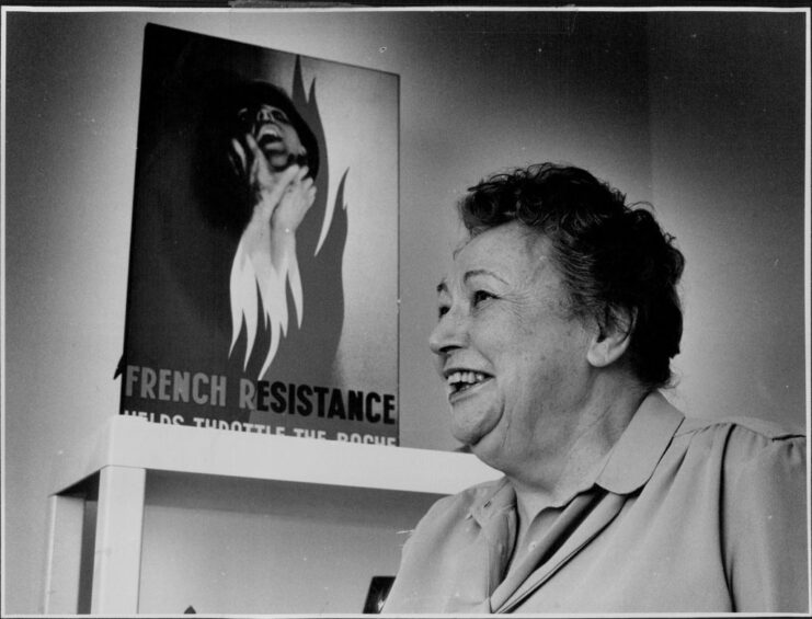 Nancy Wake standing next to a French Resistance poster