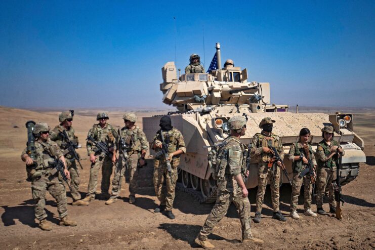 Syrian Democratic Forces (SDF) fighters and American soldiers standing around a military vehicle in the Syrian desert