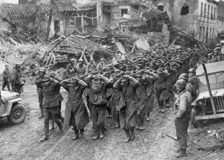 Columns of German soldiers walking down a dirt road with their hands behind their heads