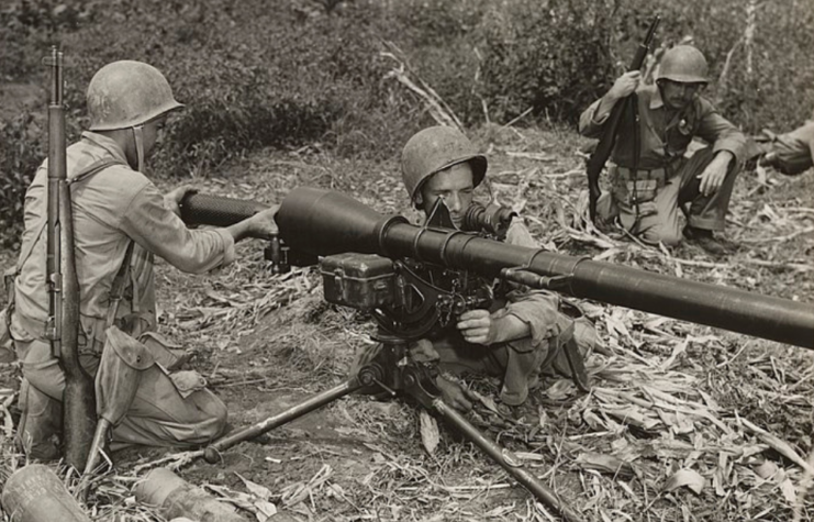 Two American soldiers loading an M20 Recoilless Rifle, while another crouches to the side with their own weapon