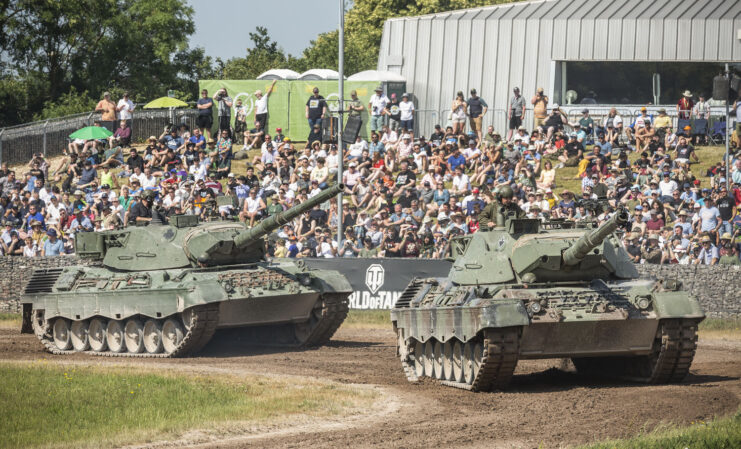 Crowd watching two tanks drive around a dirt track