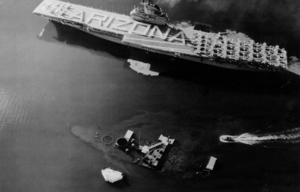 USS Bennington (CV-20) transiting past the wreckage of the USS Arizona (BB-39) with the word "ARIZONA" written on her flight deck