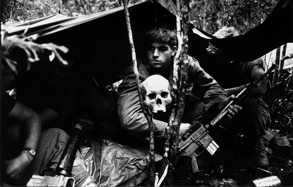American soldier sitting behind a human skull while camped out in Vietnam
