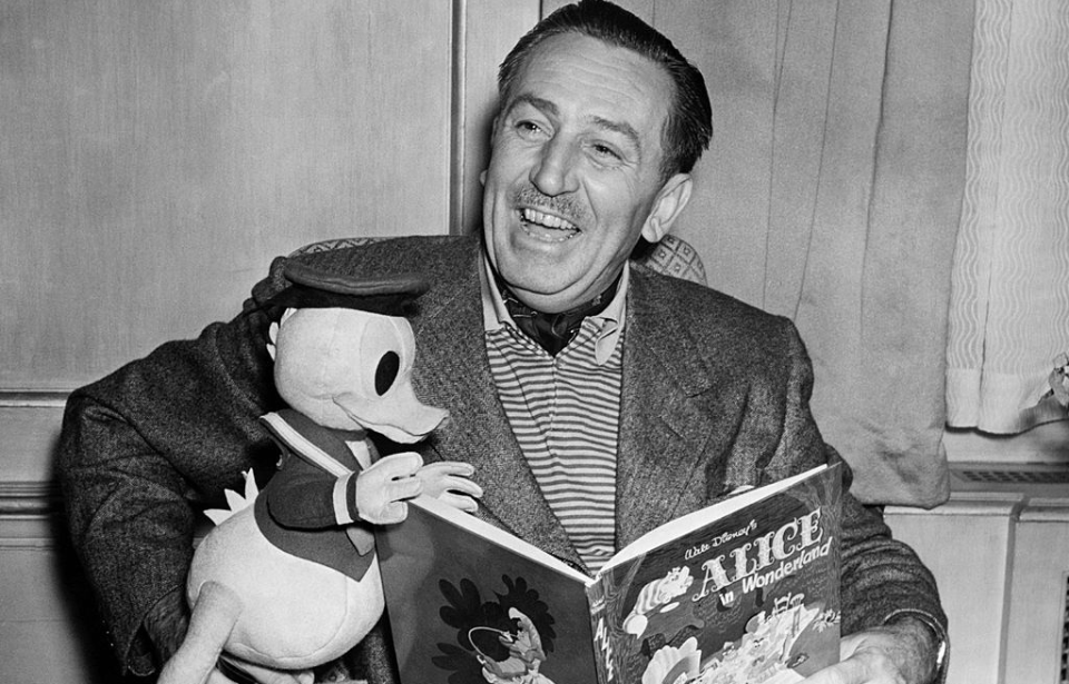 Walt Disney holding a Donald Duck plushie and a copy of the book, 'Alice In Wonderland'