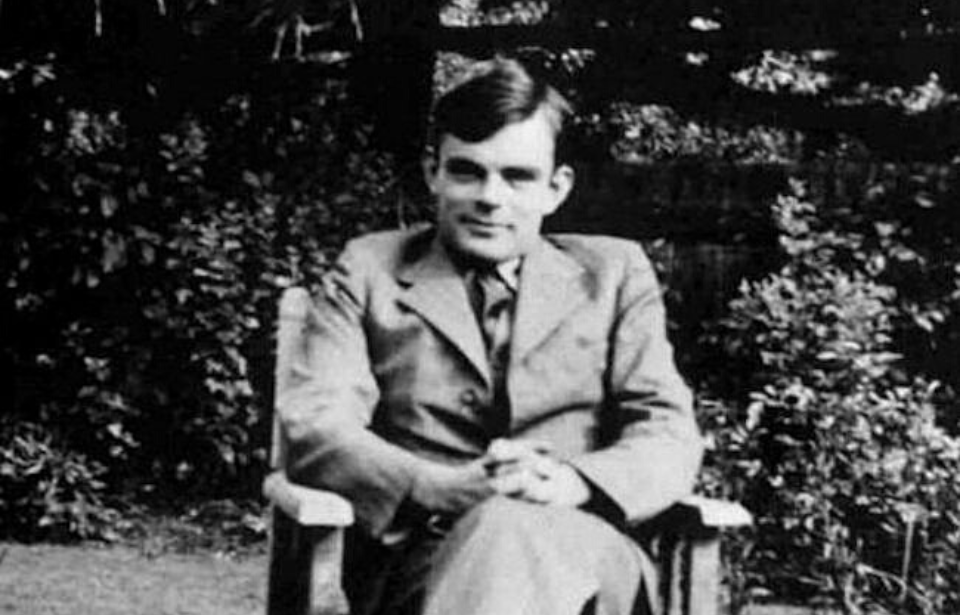 Alan Turing sitting in a chair outside