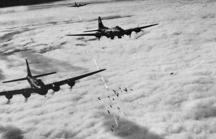 Two Boeing B-17F Flying Fortresses dropping bombs while another flies behind them in the distance