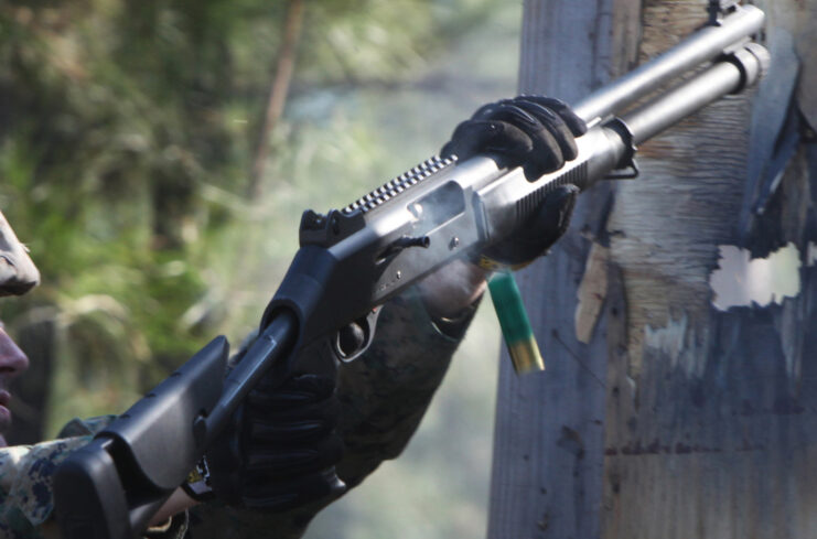 US Marine holding a Benelli M1014 through a hole in a wooden door