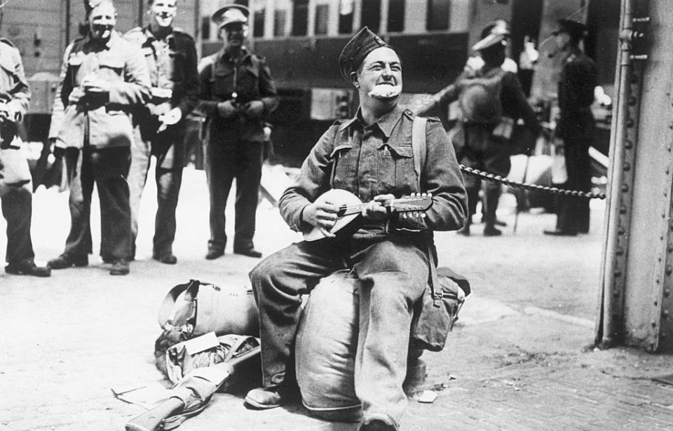 Cecil Collins playing the banjo while British soldiers walk around him