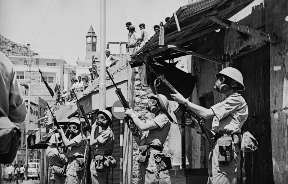 British soldiers, in gas masks, holding up their rifles