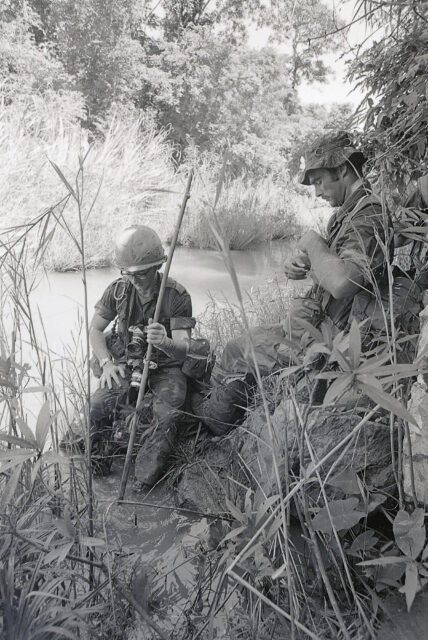 Sean Flynn and Dana Stone resting in tall grass, near a creek