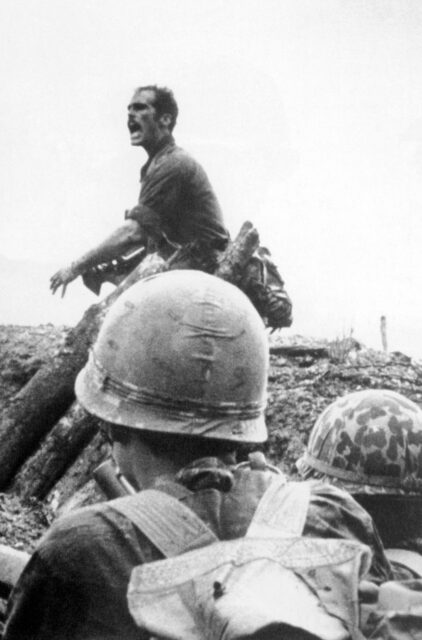 Sean Flynn yelling in the field, while American soldiers look on