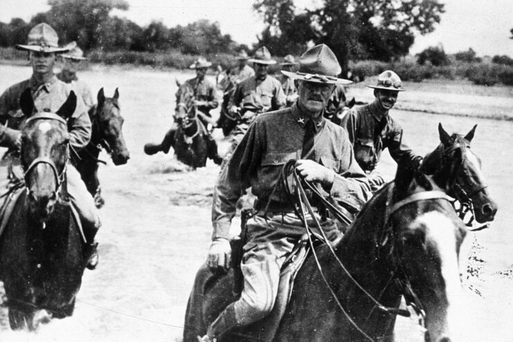 John J. Pershing and American troops riding on horseback across a river