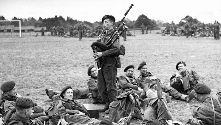 British Commandos lying on the ground while Bill Millin plays the bagpipes