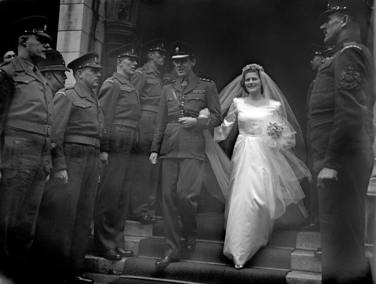 Chris and Mary Soames (née Spencer-Churchill) walking past military officers while dressed in wedding attire