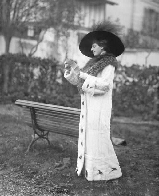 Mata Hari reading a letter while standing near a park bench